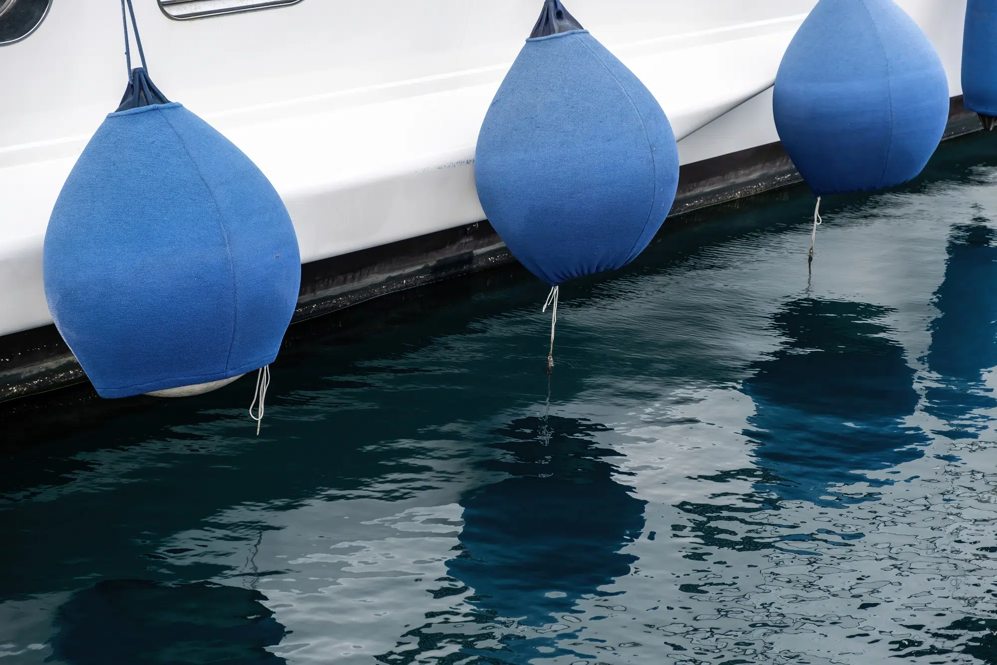 Yacht fender. Sail boat anchored at the marina detail, blue rubber bumper, reflection on sea water