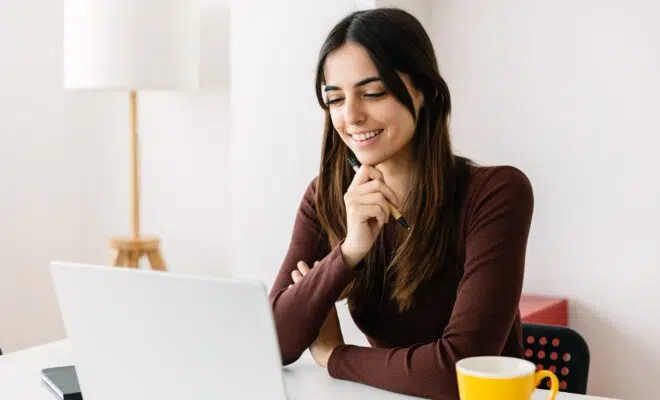 Portrait of young adult student sitting on table using laptop learning online
