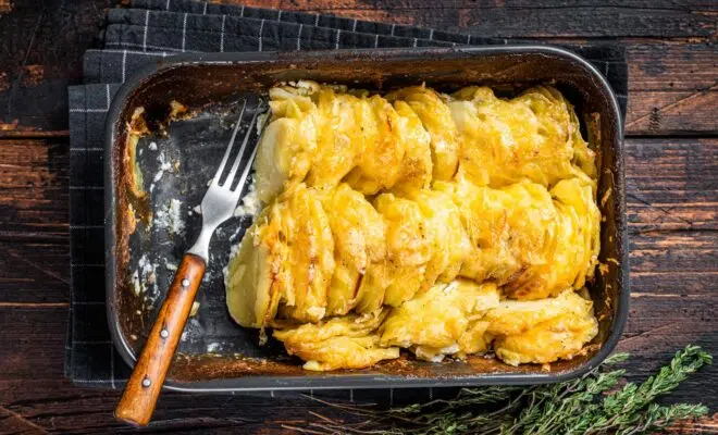 Potato casserole Gratin Dauphinois in a baking dish. Dark wooden background. Top View