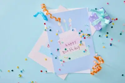 top view of colorful confetti near birthday greeting cards on blue background