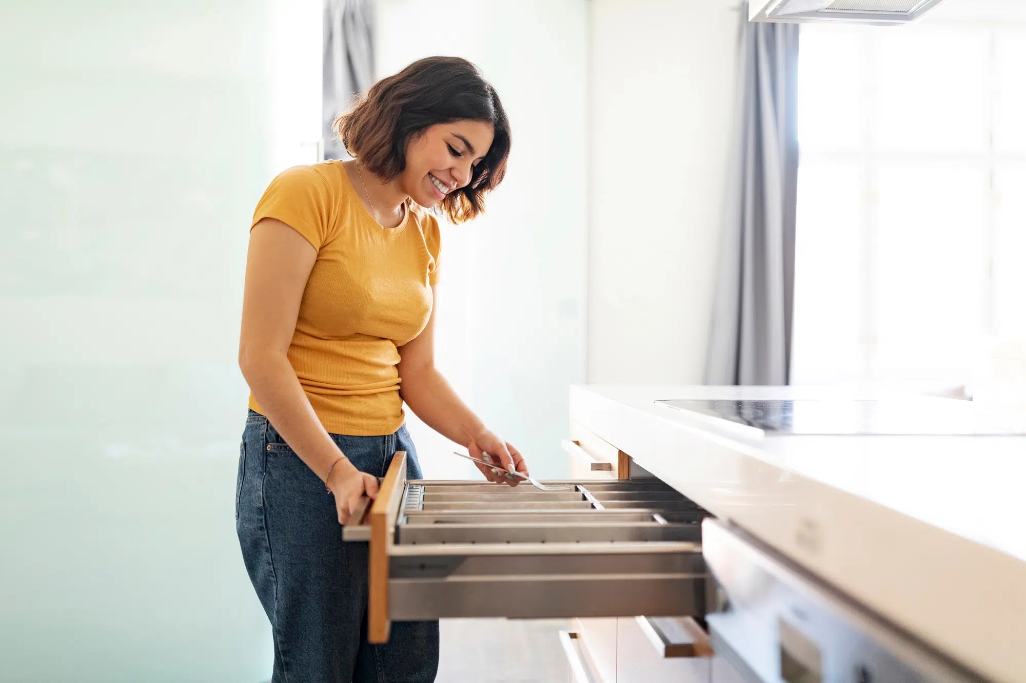 Young arab woman tidying up cutlery in drawer while cleaning in kitchen
