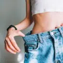 Young woman holds jeans in her hand, shows a thin waist Slim female body in large jeans