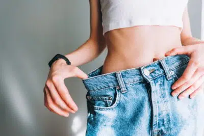 Young woman holds jeans in her hand, shows a thin waist Slim female body in large jeans