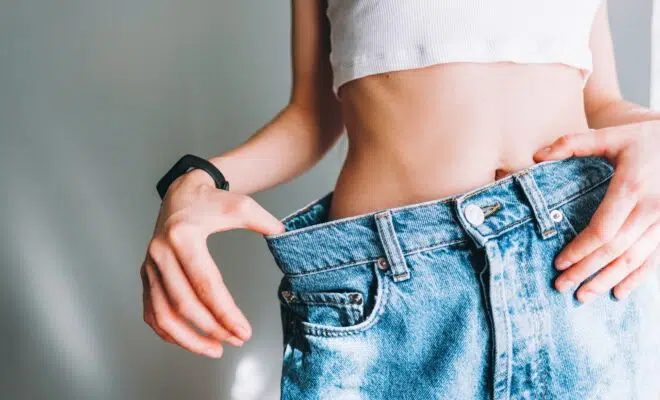 Young woman holds jeans in her hand, shows a thin waist Slim female body in large jeans